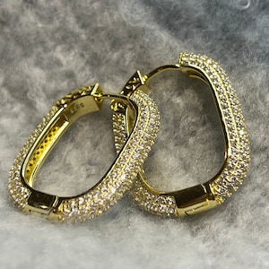 May include: A pair of gold hoop earrings with a square shape and a row of small clear stones around the edge.