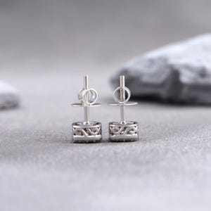 May include: A pair of silver stud earrings with a square-shaped design featuring a small cluster of clear stones.
