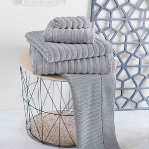 May include: A stack of grey striped bath towels on a black wire table with a woven bottom. The towels are folded and arranged in a decorative way.
