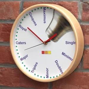 Puede incluir: Un reloj de madera con una cara de campana y una manecilla de hora roja. La esfera del reloj tiene las palabras "Maximus", "Cinques", "Royal", "Caters", "Major", "Triples", "Minor", "Doubles", "Single" y "Minimu" impresas alrededor del borde.