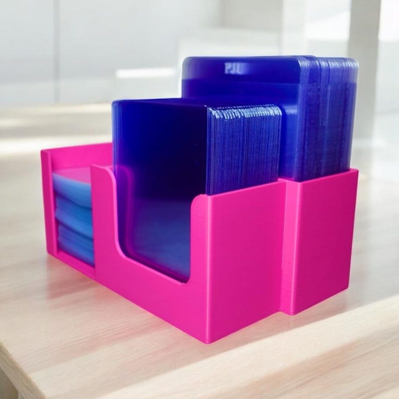 Op de afbeelding: Een felroze bureau-organizer met stapels blauwe plastic vellen. De organizer heeft drie compartimenten, met de vellen netjes gerangschikt. Het woord "PIU" is zichtbaar aan de bovenkant.