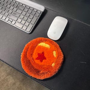 May include: An orange and yellow round rug with a red star in the center. A white computer mouse and a gray keyboard are on a black desk.