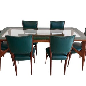 以下が含まれることがあります： ガラス天板と濃い木製フレームの長方形テーブルを備えた、ミッドセンチュリーモダン様式のダイニングセット。 6つの椅子は、ティール色の革張りの座席と背もたれでテーブルを囲み、スタイリッシュなダイニング空間を演出しています。