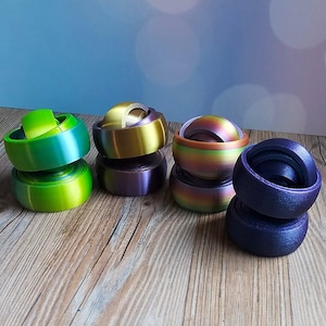 May include: A collection of colorful fidget toys in shades of green, gold, purple, and blue. Each toy has a rounded base and a spinning top. The toys are arranged on a wooden surface with a soft blue background.