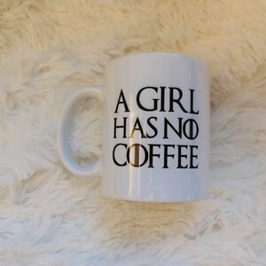 May include: White ceramic coffee mug with black text that reads "A girl has no coffee" with a stylized "Game of Thrones" inspired font.