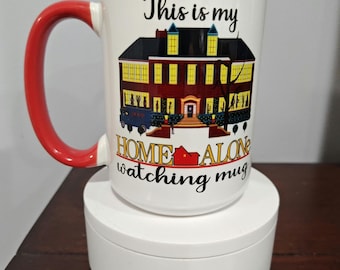 May include: White ceramic mug with a red handle. The mug has a graphic of the house from the movie Home Alone with the text "This is my Home Alone watching mug".
