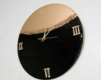May include: A black and gold resin clock with Roman numeral markings. The clock face is divided in half, with the top half being gold and the bottom half being black.