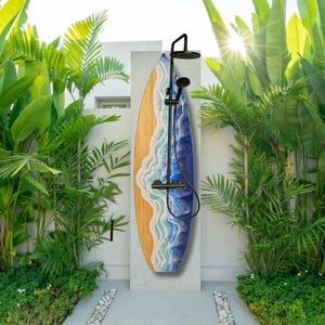 May include: A decorative outdoor shower with a surfboard design. The surfboard features a wooden grain pattern with a blue and white wave design. The shower fixtures are black and include a rain shower head and handheld shower.