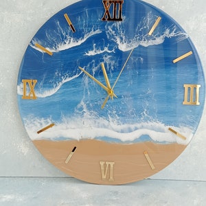 Puede incluir: Reloj de pared redondo con dise&ntilde;o de escena de playa. La esfera del reloj presenta un oc&eacute;ano azul con olas blancas y una playa de arena. N&uacute;meros romanos y manecillas doradas. Un elemento decorativo para cualquier habitaci&oacute;n, con un di&aacute;metro de unos 30 cm.