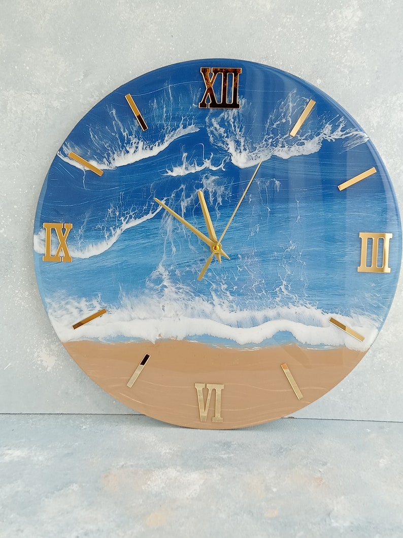 Puede incluir: Reloj de pared redondo con dise&ntilde;o de escena de playa. La esfera del reloj presenta un oc&eacute;ano azul con olas blancas y una playa de arena. N&uacute;meros romanos y manecillas doradas. Un elemento decorativo para cualquier habitaci&oacute;n, con un di&aacute;metro de unos 30 cm.