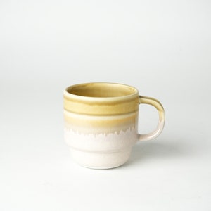 May include: A ceramic mug with a yellow and white glaze. The mug has a rounded shape and a handle.