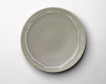 Może przedstawiać: Okrągły, ceramiczny talerz z nakrapianym, matowym wykończeniem. Talerz ma jasnozielony środek z białym i różowo-brązowym obramowaniem. Talerz jest w neutralnym kolorze i nadaje się do serwowania potraw.