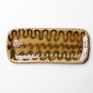 May include: A rectangular ceramic dish with a brown and yellow glaze. The dish has a decorative pattern of wavy lines and dots around the edge.