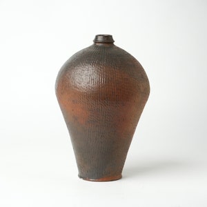 May include: A brown ceramic vase with a textured surface. The vase has a rounded body and a narrow neck.