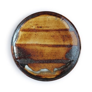 May include: A brown ceramic plate with a striped glaze pattern. The plate has a dark brown rim and a light brown center with a white glaze in the center.