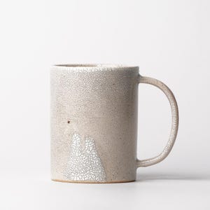 May include: A white ceramic mug with a crackled glaze and a subtle design. The mug has a rounded handle.