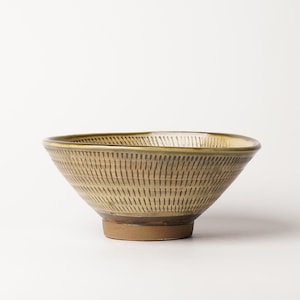 May include: A ceramic bowl with a wide, flared rim and a tapered base. The exterior features a light tan glaze decorated with a repeating pattern of vertical, dark brown etched dashes arranged in horizontal bands around the entire vessel.