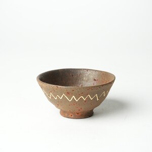 May include: A small, brown ceramic bowl with a white zig-zag pattern around the rim. The bowl has a speckled, rustic finish.