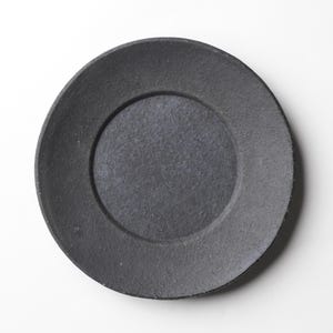 May include: A black ceramic saucer with a slightly raised rim and a smooth, matte finish.