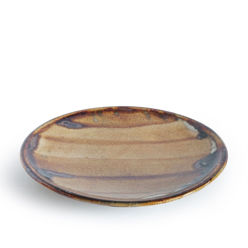 May include: A brown and beige ceramic plate with a striped design. The plate has a slightly raised rim and a glossy finish.
