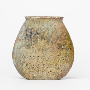 May include: A small, oval-shaped ceramic vase with a textured, mottled glaze in shades of brown, green, and white. The vase has a slightly flared rim and a rounded base.