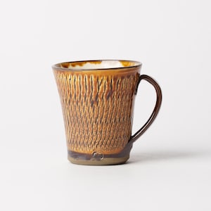 May include: A brown ceramic mug with a textured, woven pattern. The mug has a dark brown handle and rim, with a lighter brown interior. The mug is approximately 4 inches tall.