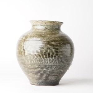 Puede incluir: Un jarrón grande de cerámica verde con una superficie texturizada y un patrón decorativo alrededor del centro.