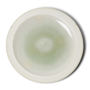 Puede incluir: Un plato redondo de cerámica blanquecina con un centro verde pálido. El centro tiene un efecto de craquelado y el borde es de un tono blanco más claro. El plato está sobre un fondo blanco.