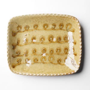 May include: A rectangular ceramic serving dish with a light brown glaze and a decorative pattern of brown loops around the edges.