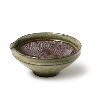 May include: A ceramic mortar bowl with a textured interior and a spout. The bowl has a brown interior and a light green exterior with a speckled finish. The bowl is designed for grinding ingredients.