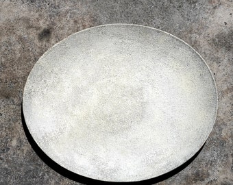 Może przedstawiać: Biały owalny talerz ceramiczny z fakturowaną powierzchnią. Talerz leży na szarej betonowej powierzchni.