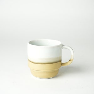 May include: A white ceramic mug with a brown and beige glaze. The mug has a rounded shape and a handle.