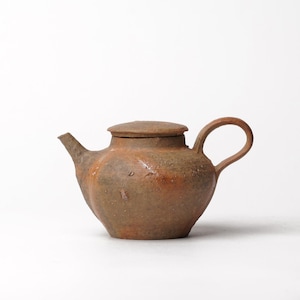 May include: A small, round, brown ceramic teapot with a textured, earthy surface. It features a short, angled spout, a curved handle, and a flat, circular lid that sits flush on top of the main body of the vessel.