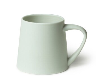 Peut inclure: Une tasse en céramique de couleur vert clair avec une anse arrondie. La tasse a une finition lisse et mate.
