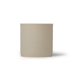 May include: A light beige ceramic mug with a rounded shape and a subtle texture. The mug has a small circle logo on the bottom.