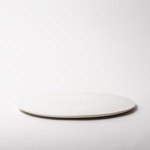 May include: A white, oval-shaped ceramic platter with a slightly textured surface. The serving dish is set against a white background, showcasing its simple, elegant design. Ideal for serving appetizers or desserts.