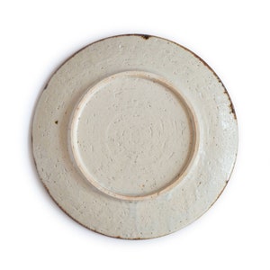 May include: A white ceramic plate with a textured surface and a brown rim. The plate is round and has a slightly raised center.