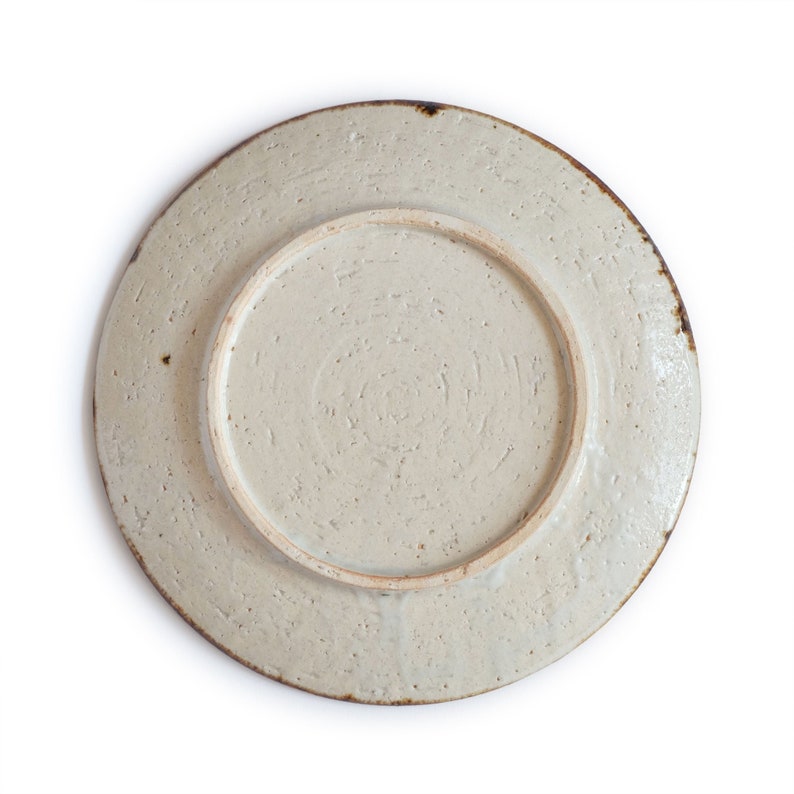 May include: A white ceramic plate with a textured surface and a brown rim. The plate is round and has a slightly raised center.