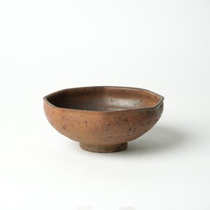 May include: A brown ceramic bowl with a slightly irregular, octagonal shape. The bowl has a speckled, textured surface and a small, rounded base.