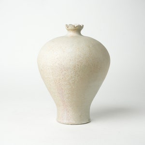 May include: A white ceramic vase with a rounded body and a slightly flared neck. The vase has a textured surface and a slightly uneven rim.