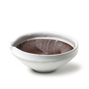 May include: White ceramic suribachi, a Japanese mortar, with a brown, textured grinding surface. The mortar has a slightly curved rim and a small spout.