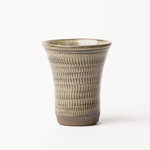 May include: A ceramic tumbler with a flared rim and a tapered base. The exterior features a textured, repeating vertical pattern in muted olive green and earthy brown tones, with a smooth, unglazed dark brown finish on the bottom section.