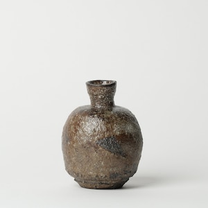 May include: A small, round, brown ceramic vase with a textured surface. The vase has a wide mouth and a narrow neck.