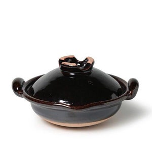 May include: A black ceramic pot with a lid. The pot has a rounded shape and a slightly flared rim. The lid has a small handle on top.