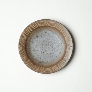 May include: A brown ceramic plate with a decorative wave pattern around the rim. The plate has a speckled glaze and a light gray interior.