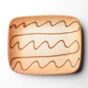 May include: A rectangular ceramic serving dish with a light brown glaze and a decorative brown wavy line pattern.
