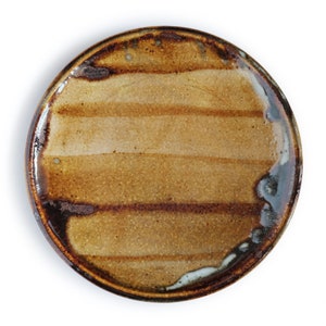 May include: A brown ceramic plate with a striped design. The plate has a dark brown rim and a light brown center with brown stripes.