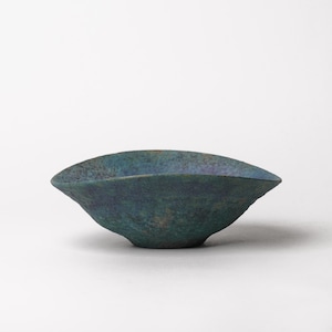 May include: A shallow, wide-rimmed bowl with a textured, mottled surface featuring deep shades of teal, blue, and hints of dark brown. The bowl has an irregular, organic shape with a slightly uneven rim and a tapered base, showcasing a matte finish.