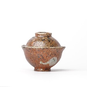 May include: A small, brown and white ceramic pot with a lid. The pot has a speckled glaze and a rounded shape.