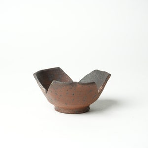 May include: A small, brown ceramic bowl with a unique, five-pointed star shape. The bowl has a speckled, rustic finish.